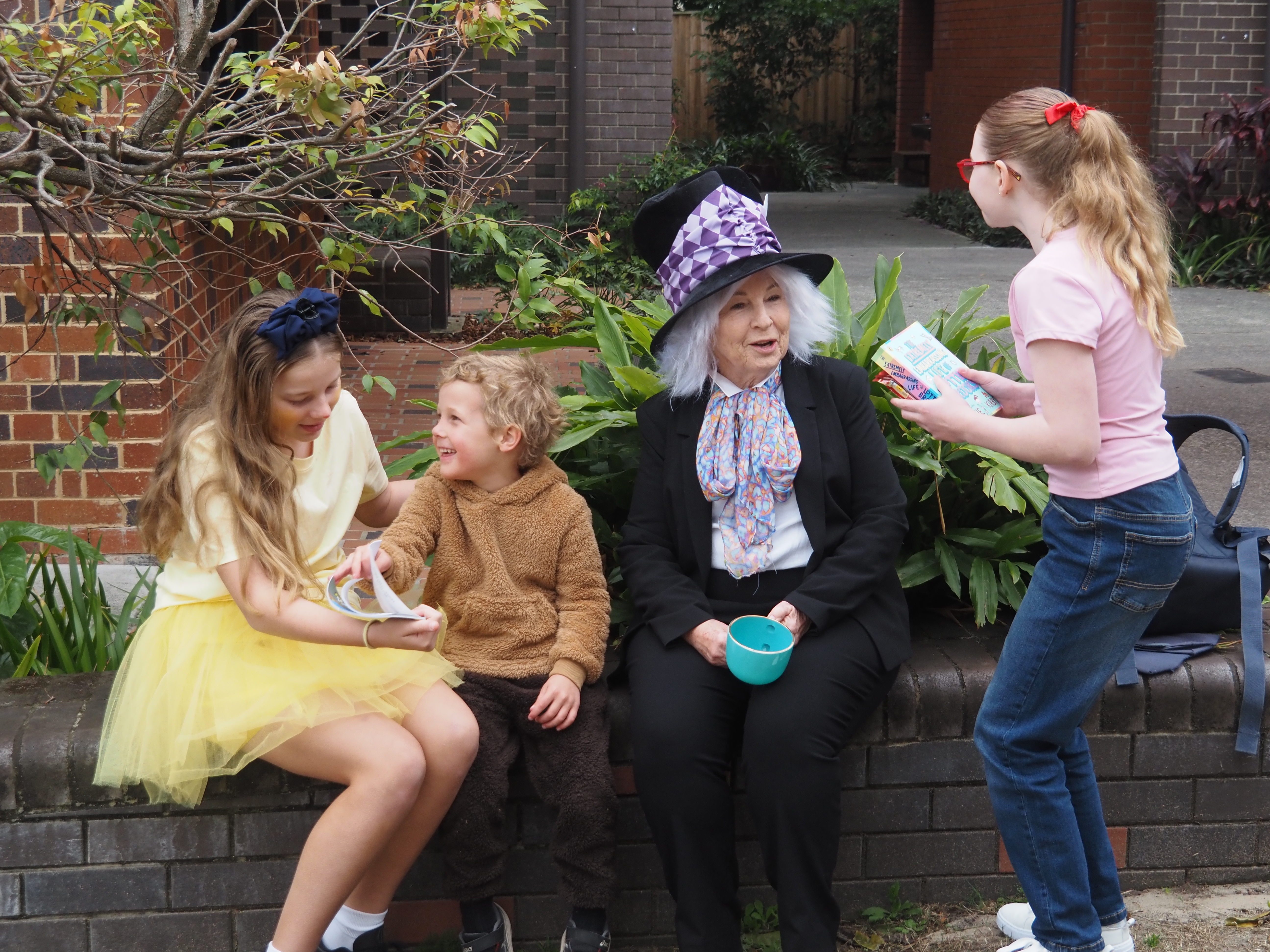 Students and an adult taking part in a school dress‑up reading activity outdoors.
