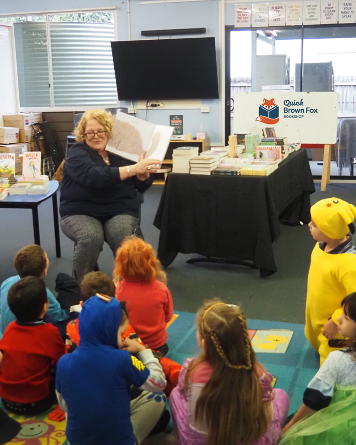 Storytime session with students listening to an adult reading a picture book in a classroom.