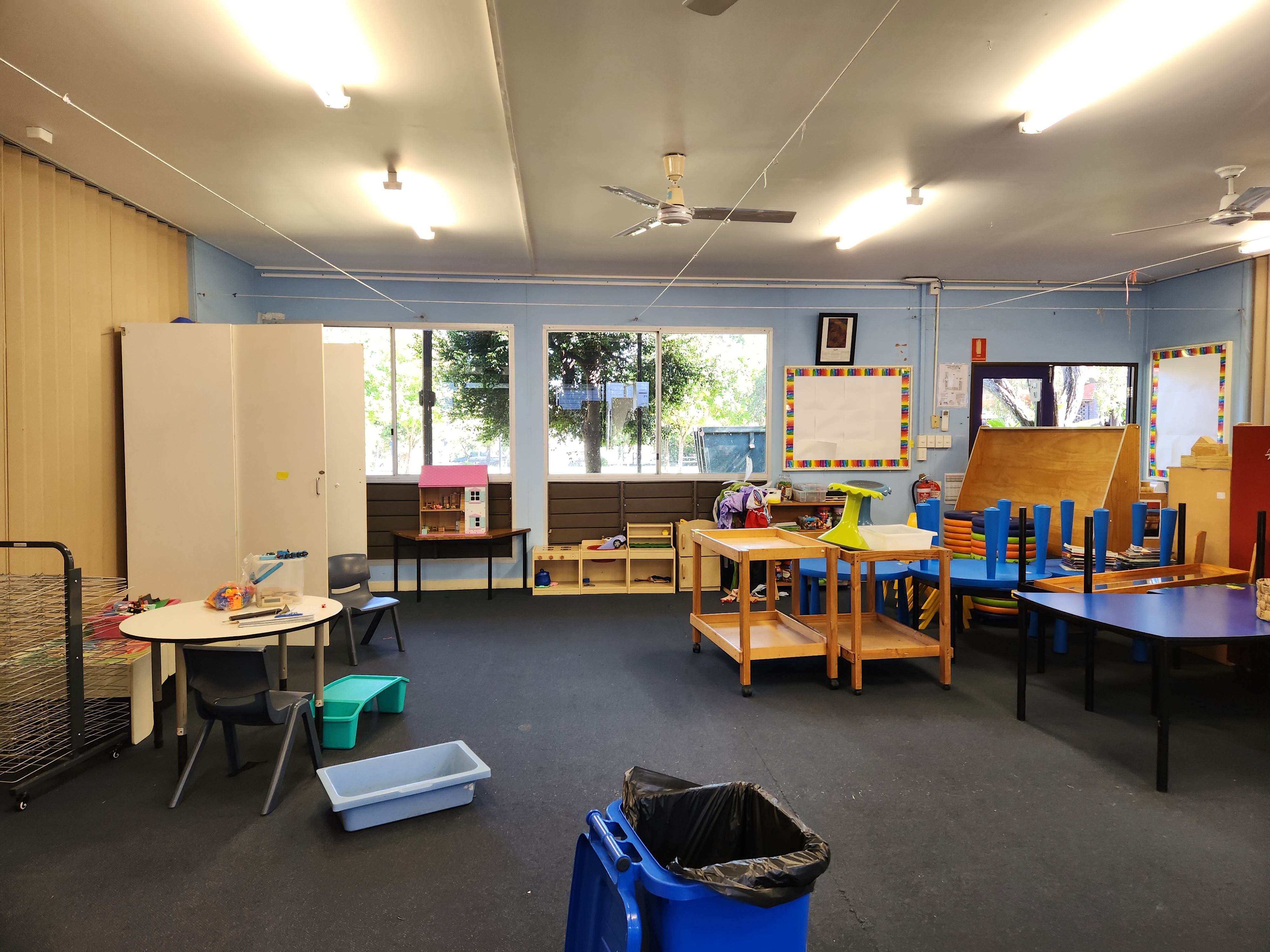 Empty classroom set up for early learning, with tables, chairs, shelves, and play equipment.
