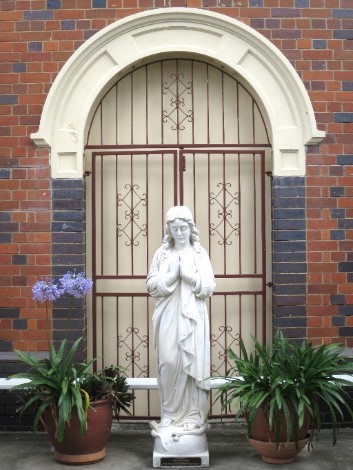 Religious statue of Mary positioned in front of a brick building entrance.